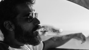 Un chico con barba fumando en un coche